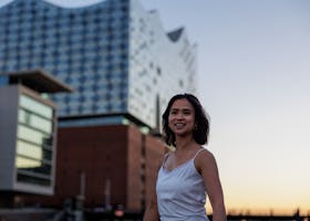 A smiling woman poses in front of Hamburg's Elbphilharmonie during sunset, capturing the architectural beauty.